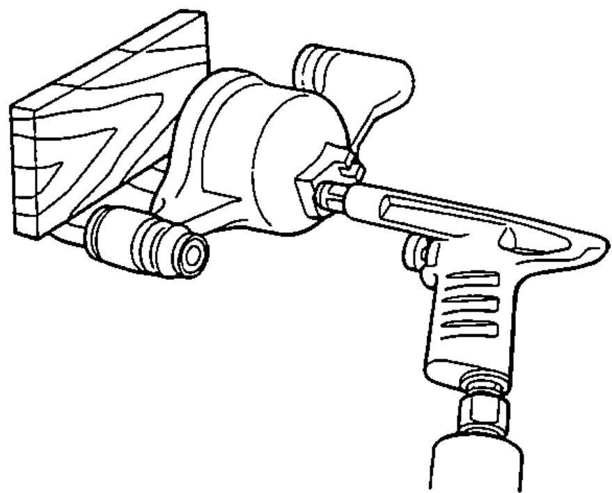 Caliper held against a wooden block while an air nozzle applies compressed air through the brake line hole to push the piston out.