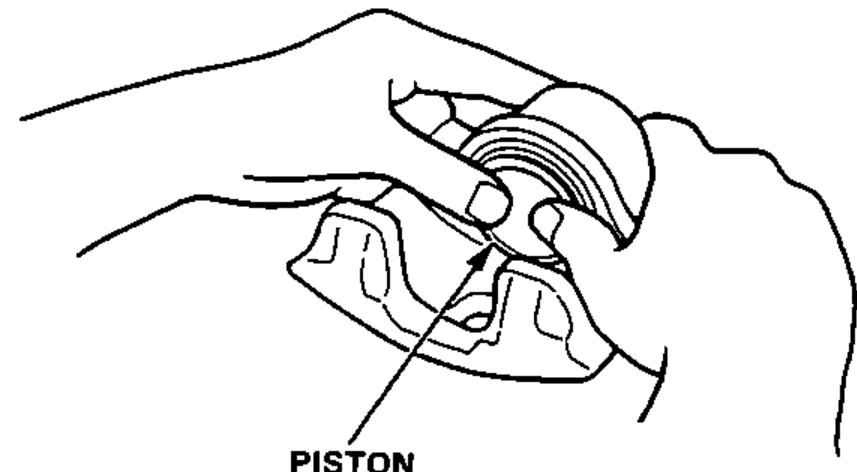 Hands installing the piston into the caliper cylinder with the dished end facing in.